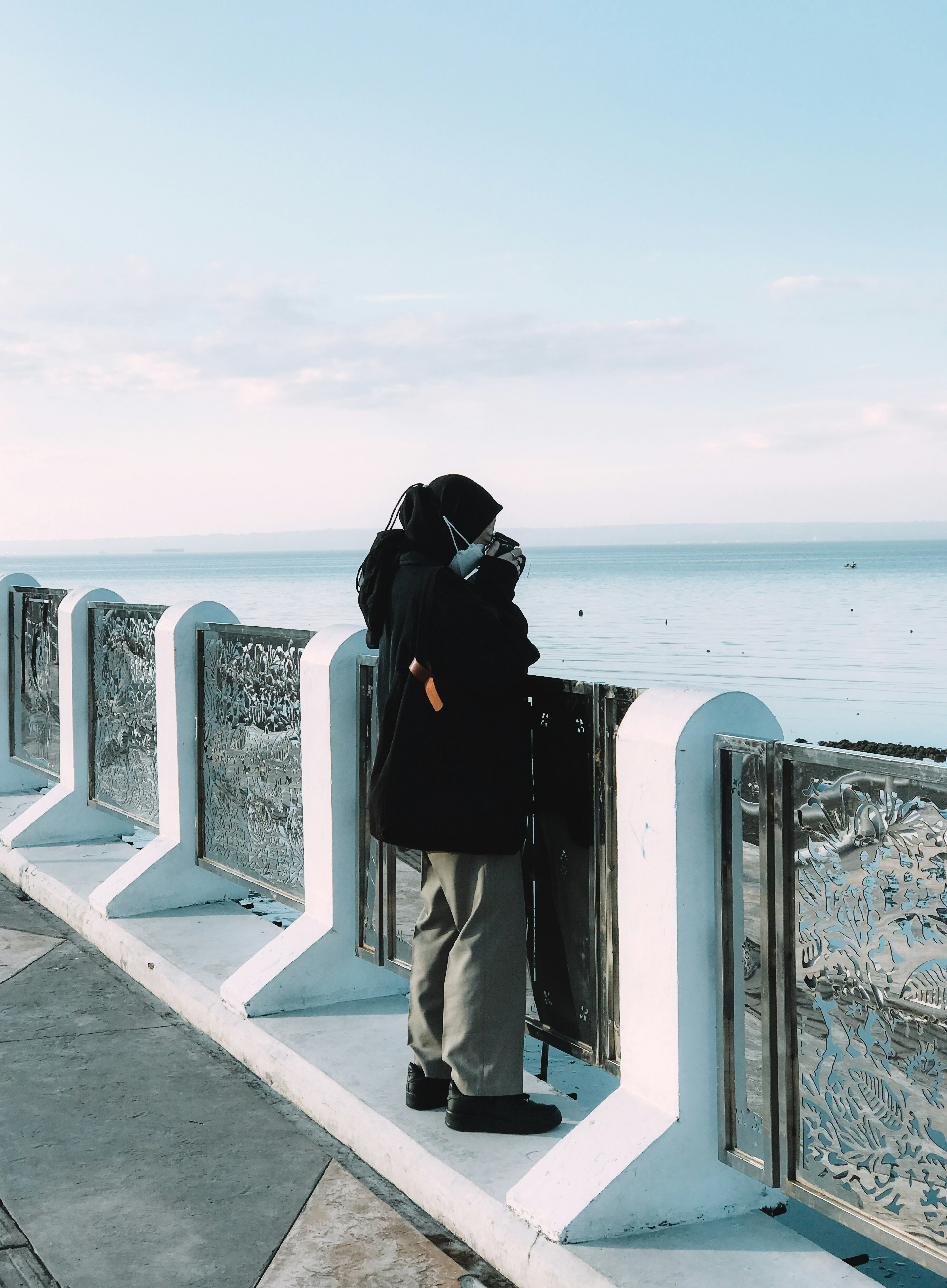 man in black hoodie and gray pants standing on gray concrete dock during daytime